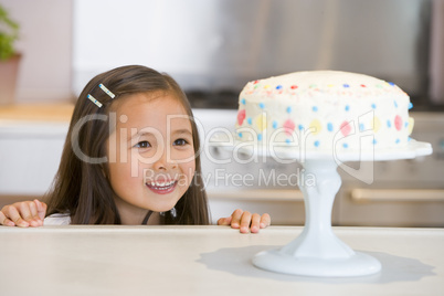 Young girl at kitchen counter looking at cake smiling