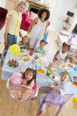 Young children at party with mothers sitting at table with food
