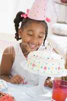 Young girl wearing party hat looking at cake smiling