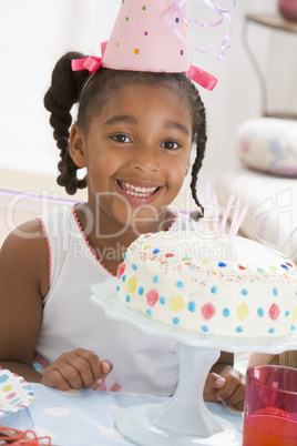 Young girl wearing party hat with cake in front of her smiling