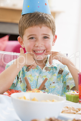 Young boy at party sitting at table with food smiling