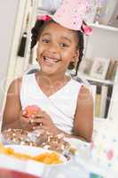Young girl at party sitting at table with a cupcake smiling