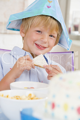 Young boy at party sitting at table with a sandwich smiling