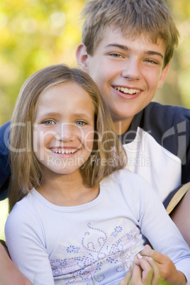Brother and sister sitting outdoors smiling
