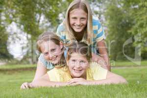 Three young girl friends piled on each other outdoors smiling