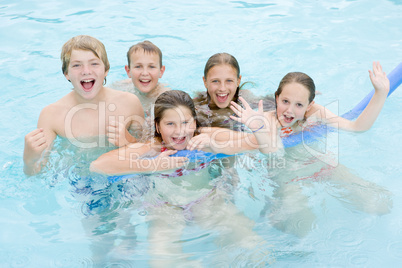 Five young friends in swimming pool playing and smiling