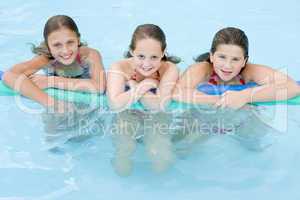 Three young girl friends in swimming pool with pool noodle smili