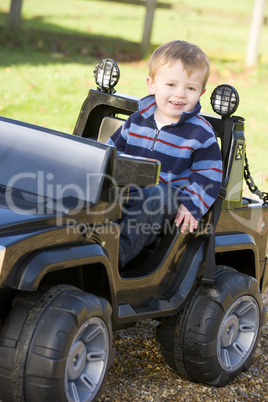 Young boy playing outdoors in toy truck smiling