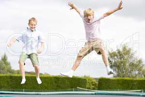 Two young boys jumping on trampoline smiling