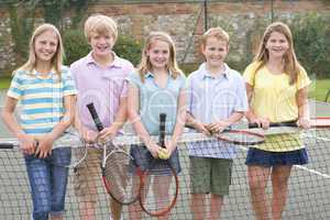 Five young friends with rackets on tennis court smiling