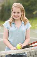 Young girl with racket on tennis court smiling