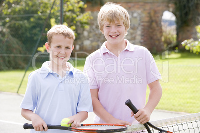 Two young male friends with rackets on tennis court smiling