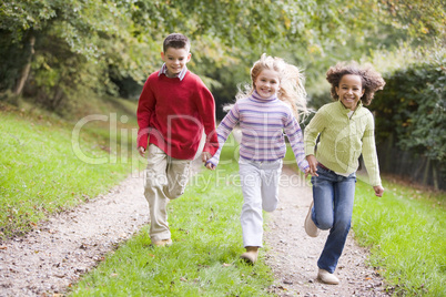 Three young friends running on a path outdoors smiling