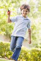 Young boy with toy airplane running outdoors smiling