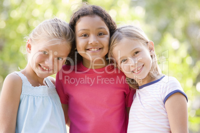 Three young girl friends standing outdoors smiling
