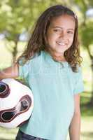 Young girl holding soccer ball outdoors smiling