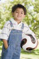 Young boy holding soccer ball outdoors smiling