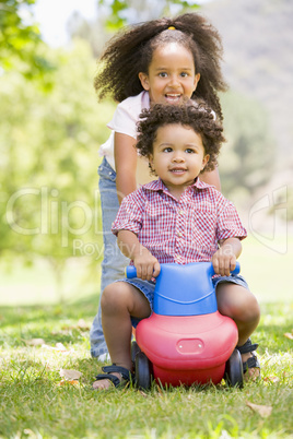 Sister pushing brother on toy with wheels smiling