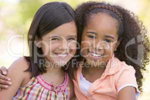 Two young girl friends sitting outdoors smiling