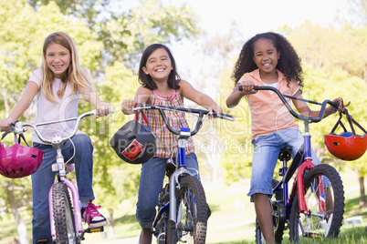 Three young girl friends outdoors on bicycles smiling