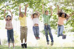 Five young friends jumping outdoors smiling