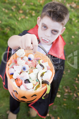 Young boy outdoors wearing vampire costume on Halloween holding