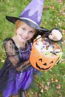 Young girl outdoors in witch costume on Halloween holding candy