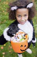 Young girl outdoors in cat costume on Halloween holding candy