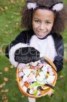Young girl outdoors in cat costume on Halloween holding candy