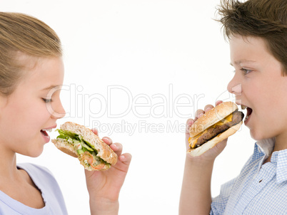 Sister eating apple by brother eating cheeseburger