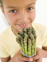 Young girl holding bunch of asparagus and smiling
