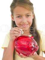 Young girl putting coin into piggy bank smiling