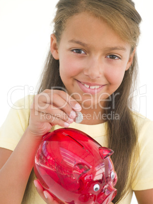 Young girl putting coin into piggy bank smiling