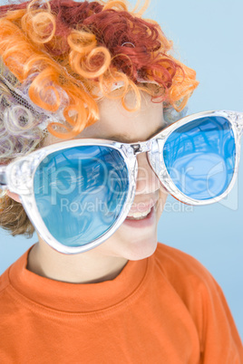 Young boy wearing clown wig and sunglasses smiling