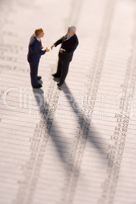 Figurines Of Two Businessmen Shaking Hands On A Financial Newspaper