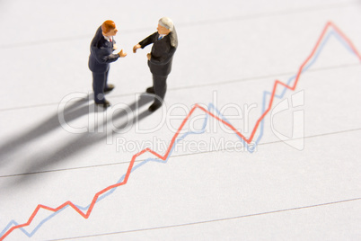 Figurines Of Two Businessmen Shaking Hands On A Line Graph