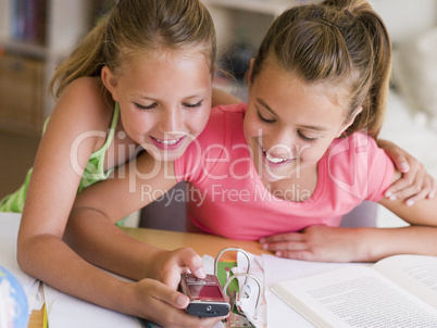 Young Girls Distracted From Their Homework, Playing With A Cellp