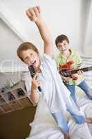 Two Boys Standing On A Bed, Playing Guitar And Singing Into A Ha