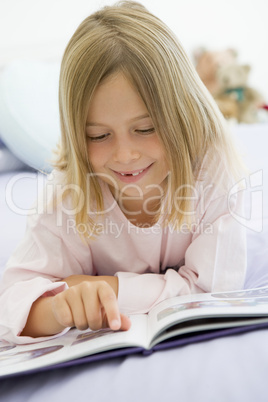 Young Girl Lying On Her Bed In Her Pajamas, Reading A Book