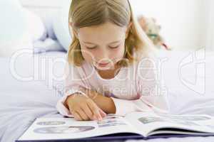 Young Girl Lying On Her Bed In Her Pajamas, Reading A Book