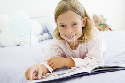 Young Girl Lying On Her Bed In Her Pajamas, Reading A Book