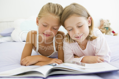 Two Young Girls In Their Pajamas, Reading A Book