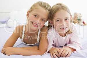 Two Young Girls In Their Pajamas Lying On A Bed