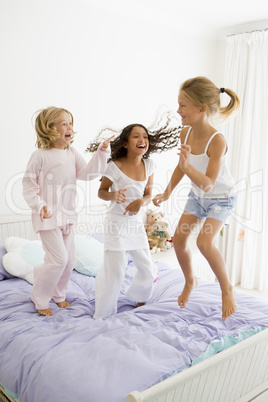 Three Young Girls Jumping On A Bed In Their Pajamas