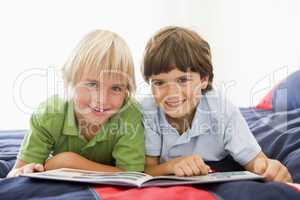 Two Young Boys Lying Down On A Bed Reading A Book