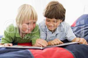 Two Young Boys Lying Down On A Bed Reading A Book