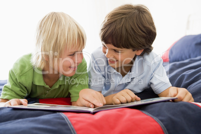 Two Young Boys Lying Down On A Bed Reading A Book