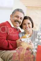 Middle Aged Couple Sitting On Sofa Holding Christmas Present