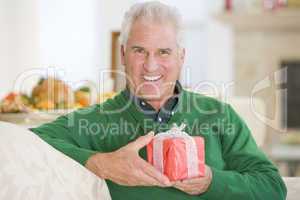 Senior Man Sitting On Sofa Holding A Christmas Gift