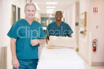 Two Orderlies Pushing An Empty Bed Down A Hospital Corridor